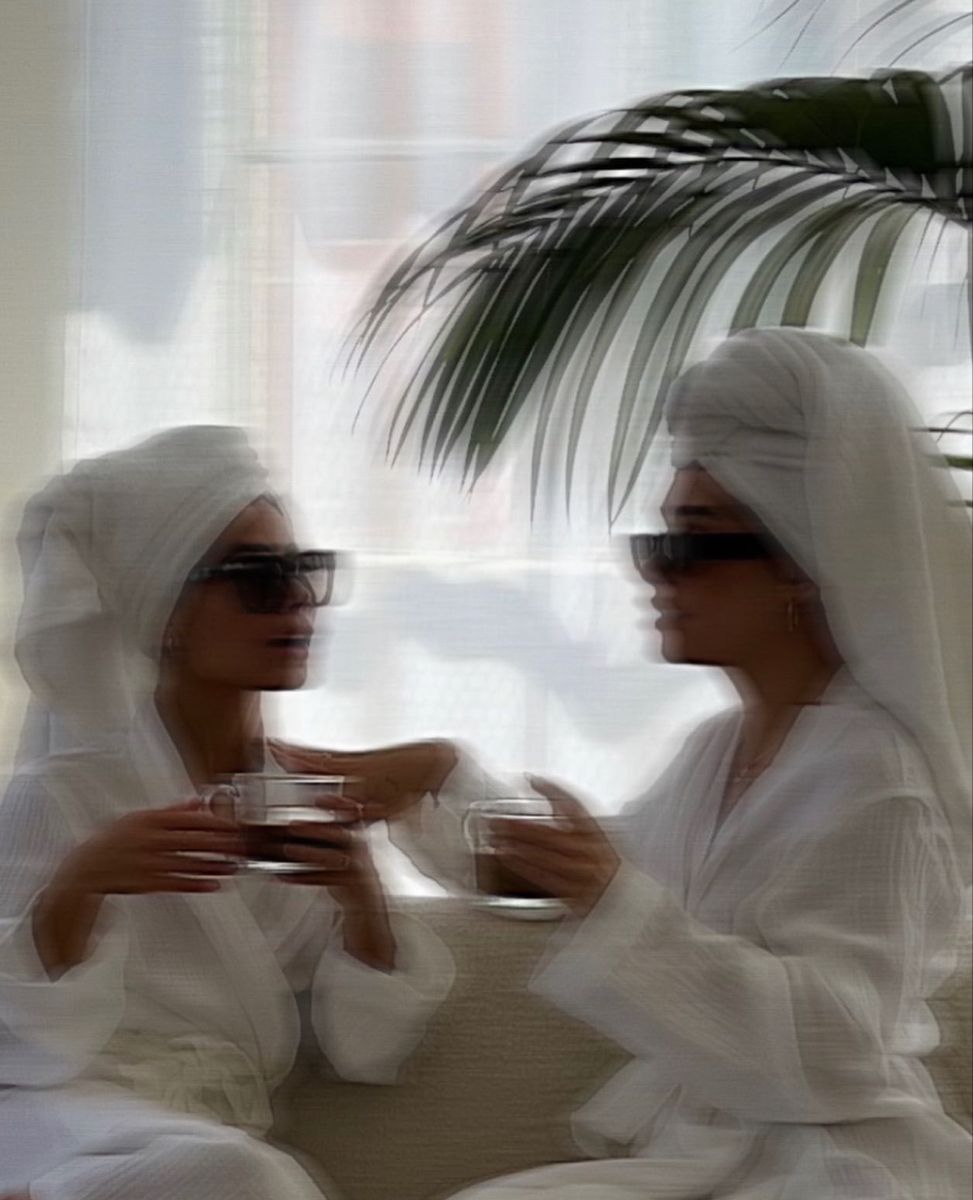 Two women in white robes and towel wraps sharing tea